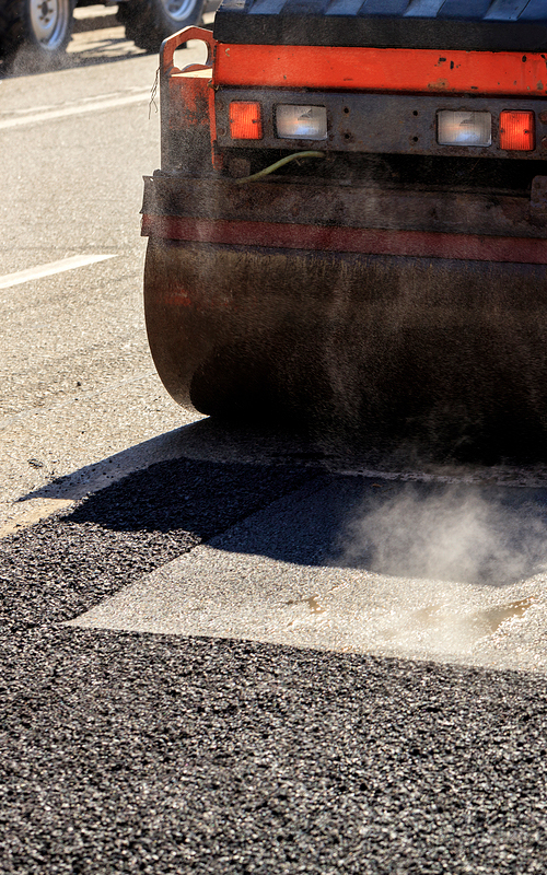 A heavy vibratory road roller compacts asphalt on the road to be repaired.